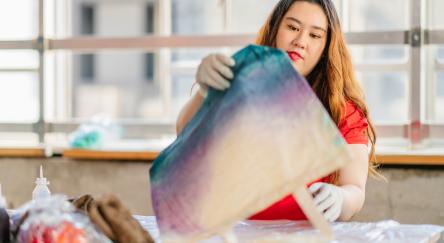 A young woman is making tie dye tote bag indoors.