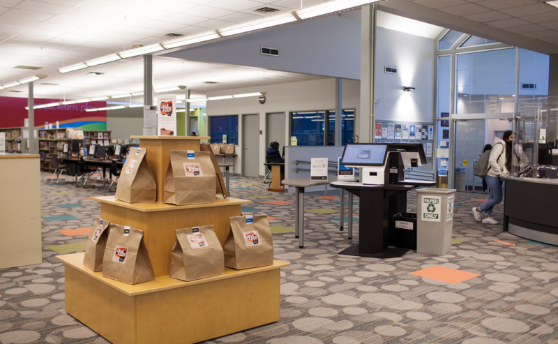 Inside George Mackie Library, showcasing self-check out kiosks and library main entrance with information desk.