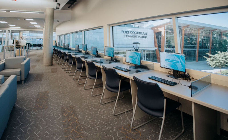 Interior of Terry Fox Library featuring computers and chairs arranged in front of large windows.