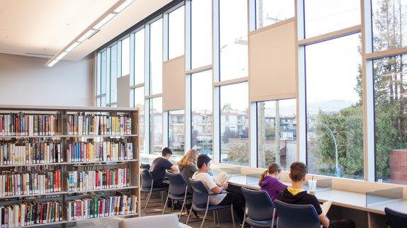 Readers in the library's desk facing a wide window.