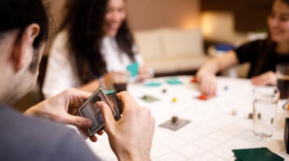 A man focused on his hand of cards, enjoying a table game with a smile on his face, surrounded by two friends.