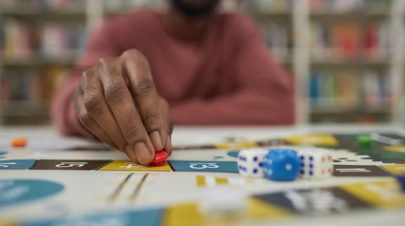 A young African American Man (20s) plays a board game on a table in the library.