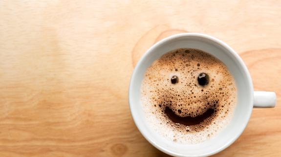 A steaming mug of coffee that has a smiley face in the crema on top.