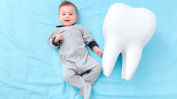 Infant child laying on blue background beside a giant tooth prop.