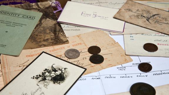 Various genealogical items, including old photos, identity cards, and family tree are displayed in an array on a table.