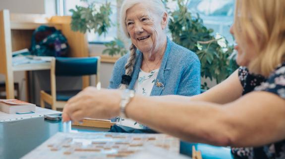 Older woman (70s) and younger woman (50s) play Scrabble together in the libarary.