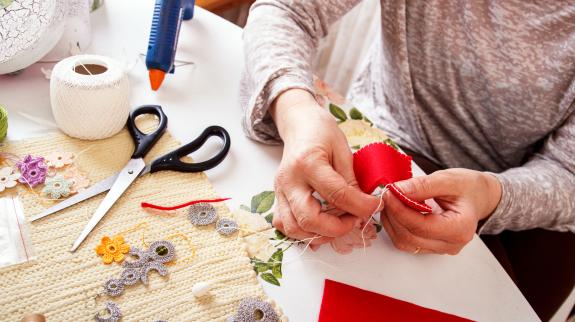 Senior women sews by hand and making heart shape ornament.