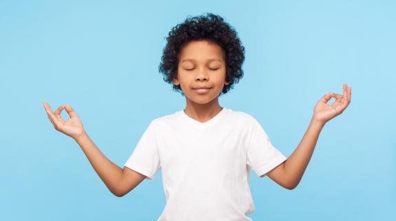 Portrait of peaceful cute little boy holding fingers in mudra gesture and meditating with closed eyes, feeling calm positive and relaxed, yoga practice.