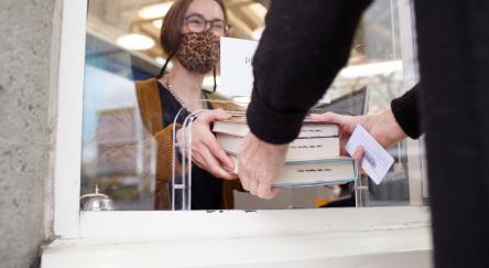 A librarian is handing books back to a customer through a drive-through window.