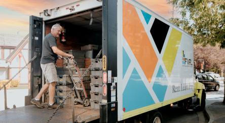 A man is seen loading boxes of library materials into a truck, readying for a delivery.