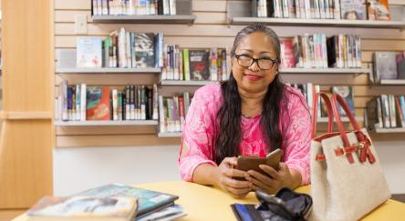 A woman sits at a library table, focused on her work, with her purse beside her.