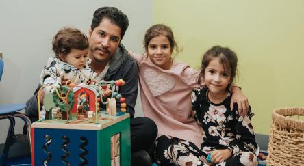 A joyful scene of a man and two kids sitting on the floor, happily playing with a bright toy between them.