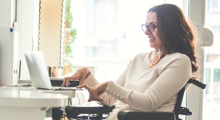 A woman using a laptop while seated in her wheelchair, representing empowerment and accessibility in the digital age.
