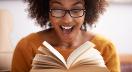 A young woman is looking at an open book with an expression of amazement on her face.