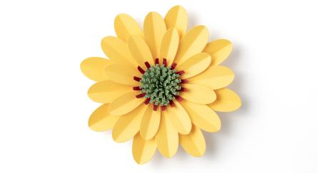 Handmade yellow flower with purple and green centre on white background.