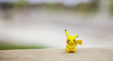 Pokemon Go character Pikachu, standing on top of a wall outdoors, in front of a defocused street.