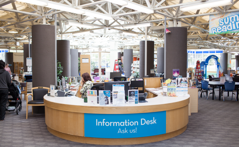  A large circular information desk in the interior of Chilliwack Library, surrounded by bookshelves and cozy reading areas.