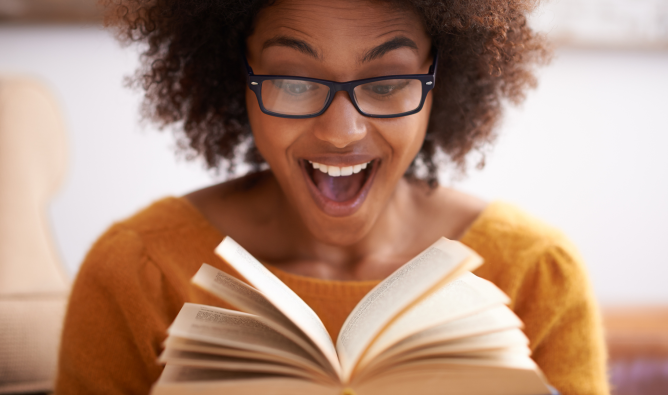 A young woman is looking at an open book with an expression of amazement on her face.